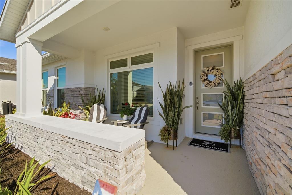 A covered front porch features stone walls, a sage green door, and two potted plants — 31477 WESTBURY ESTATES AVENUE, WESLEY CHAPEL, FL