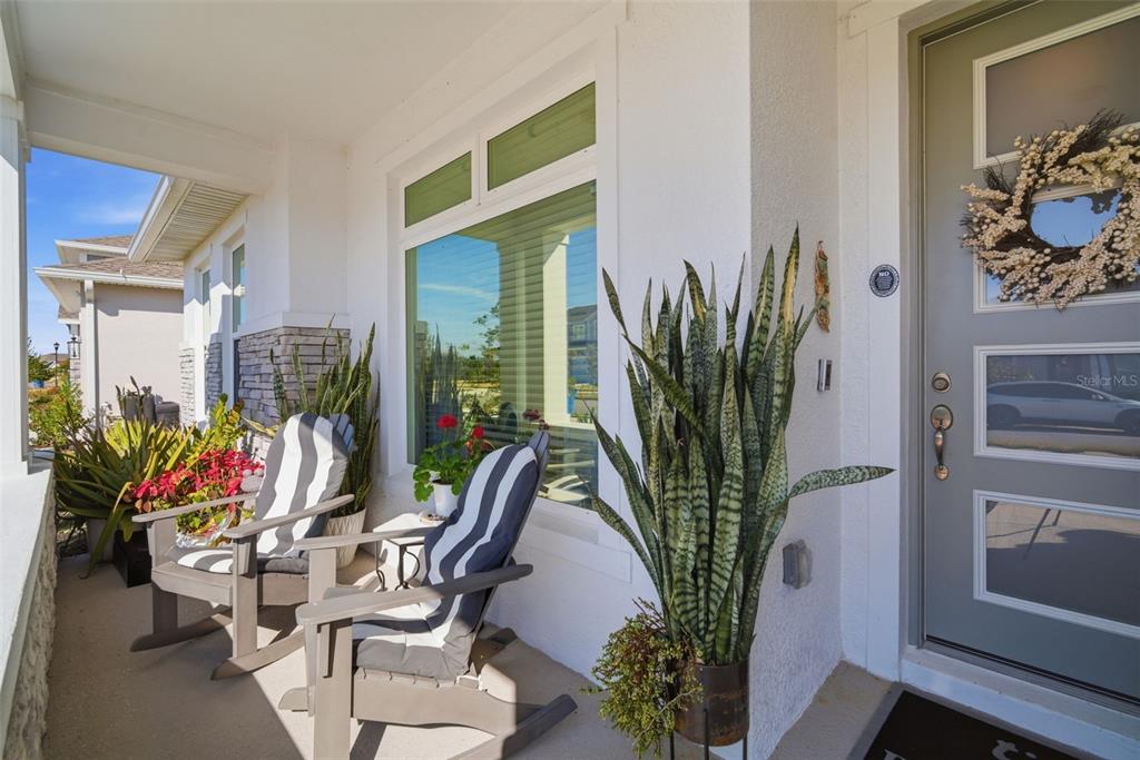A covered front porch features two rocking chairs, potted plants, and a gray front door — 31477 WESTBURY ESTATES AVENUE, WESLEY CHAPEL, FL