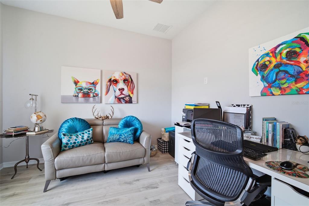 A home office features a gray loveseat, a desk with a chair, and colorful animal artwork — 31477 WESTBURY ESTATES AVENUE, WESLEY CHAPEL, FL