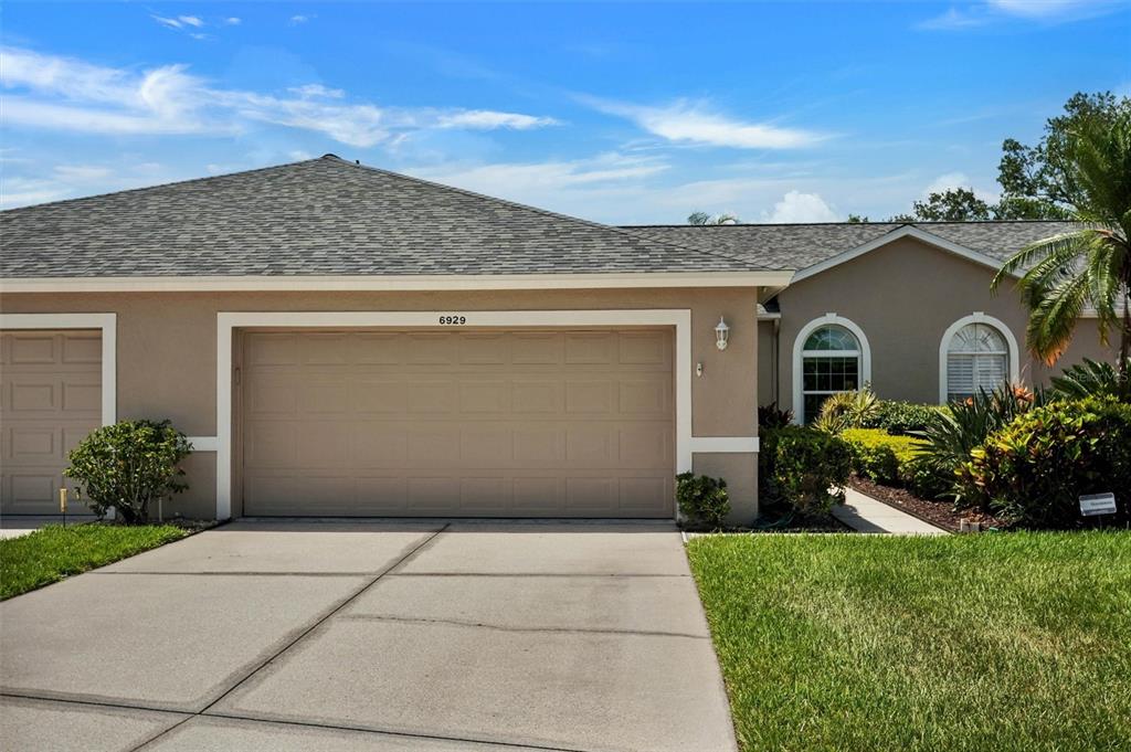 A beige house exterior features a two-car garage, a concrete driveway, and arched windows — 6929 STONEYWALK COURT, BRADENTON, FL
