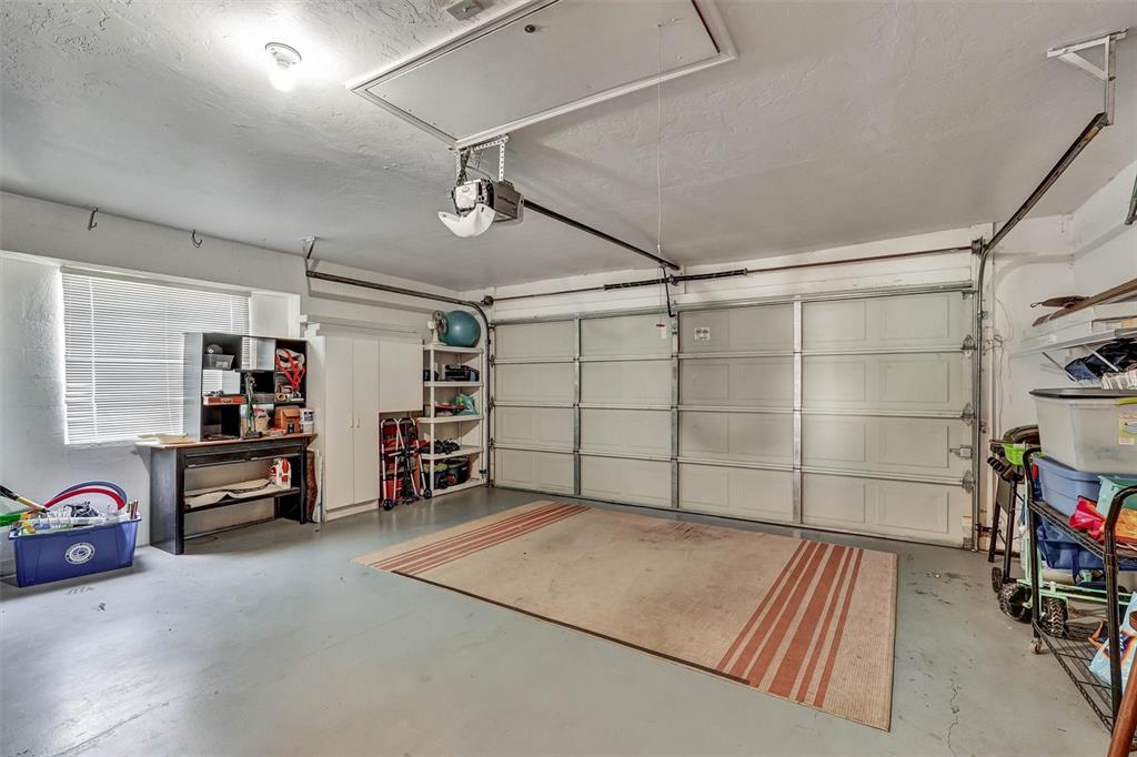 A two-car garage with a concrete floor, a large area rug, and storage shelving — 6929 STONEYWALK COURT, BRADENTON, FL