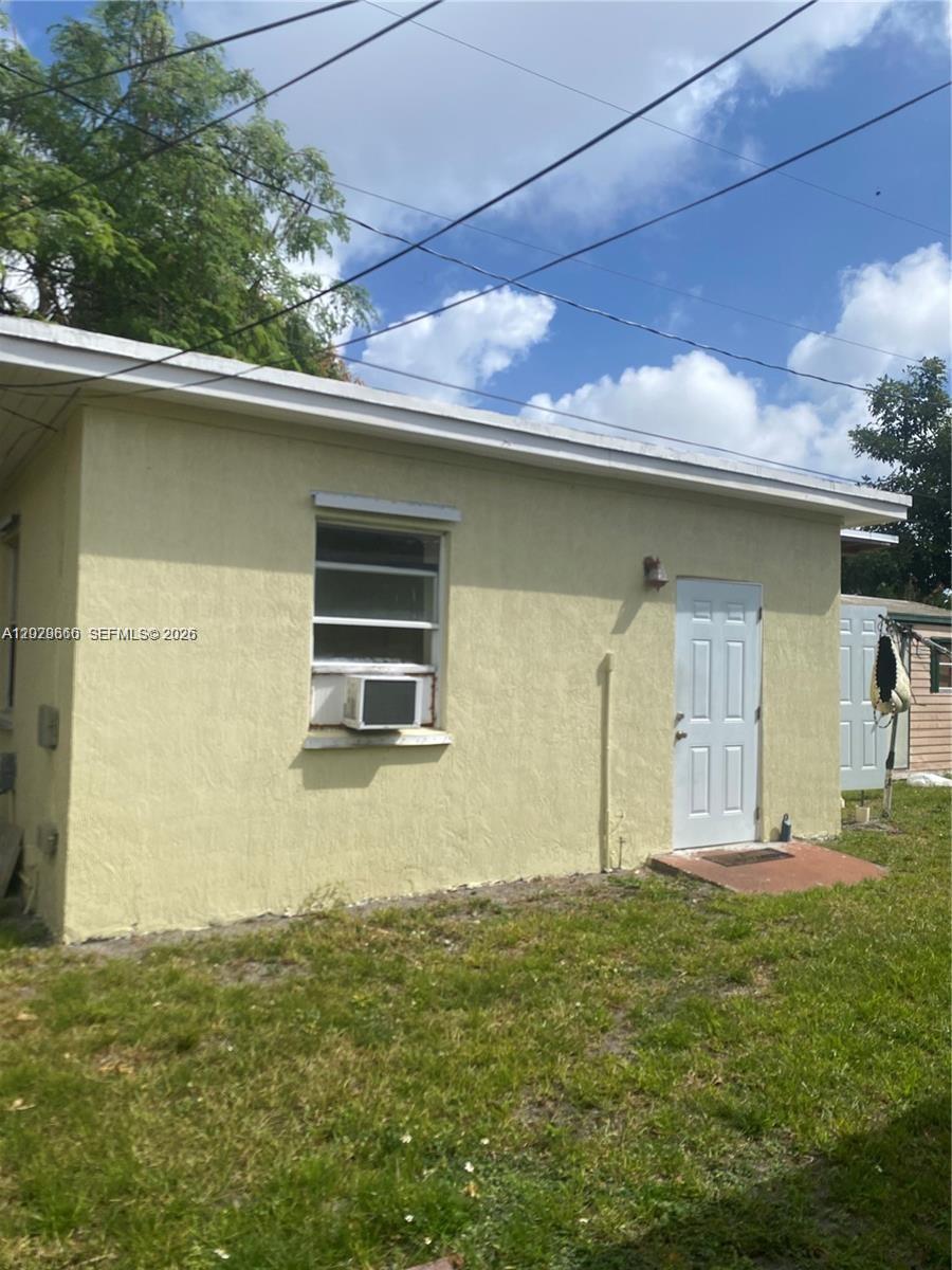 The exterior of a yellow stucco building features a white door and a window unit — 115 NE 192nd St # 1, Miami FL 33179, MIAMI, FL