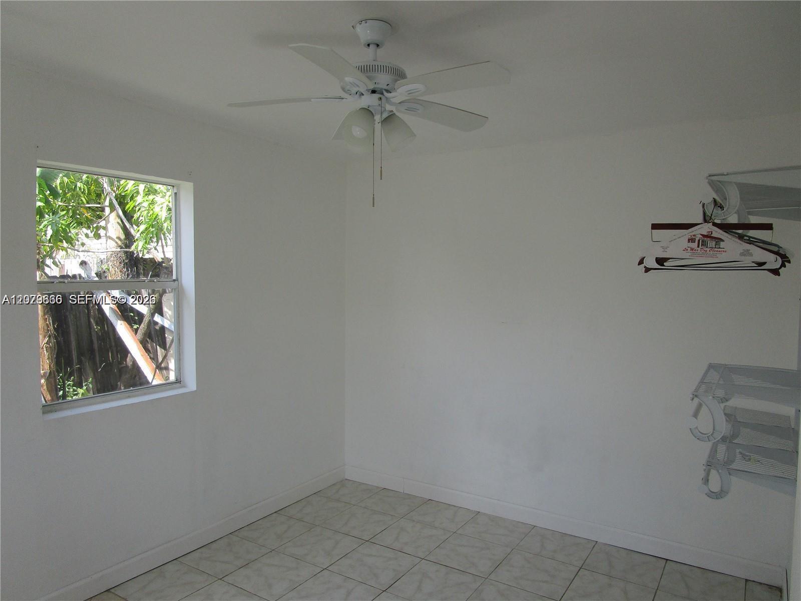 An empty room features white walls, tiled flooring, a ceiling fan, and a window — 115 NE 192nd St # 1, Miami FL 33179, MIAMI, FL