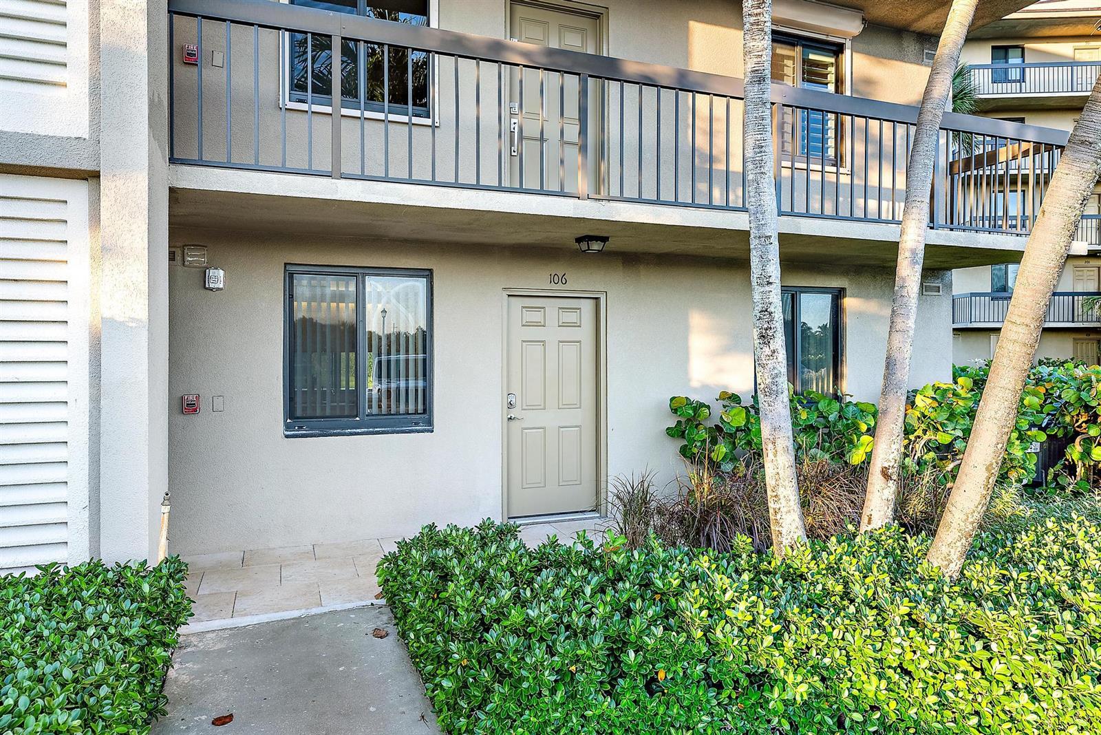 The exterior of a two-story apartment building features a ground-level entrance labeled 106 — 601 S Seas Drive # 106, Jupiter FL 33477, JUPITER, FL