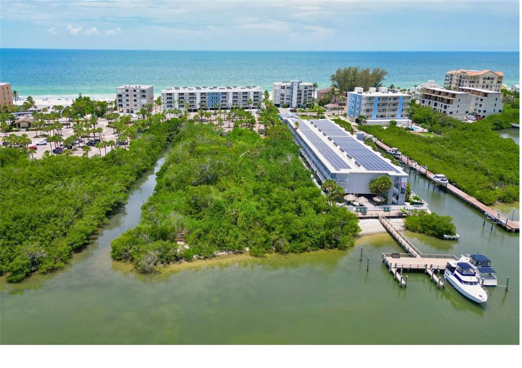 An aerial view shows a coastal building with solar panels, a boat dock, and vegetation — 19610 GULF BOULEVARD UNIT 206, INDIAN ROCKS BEACH, FL