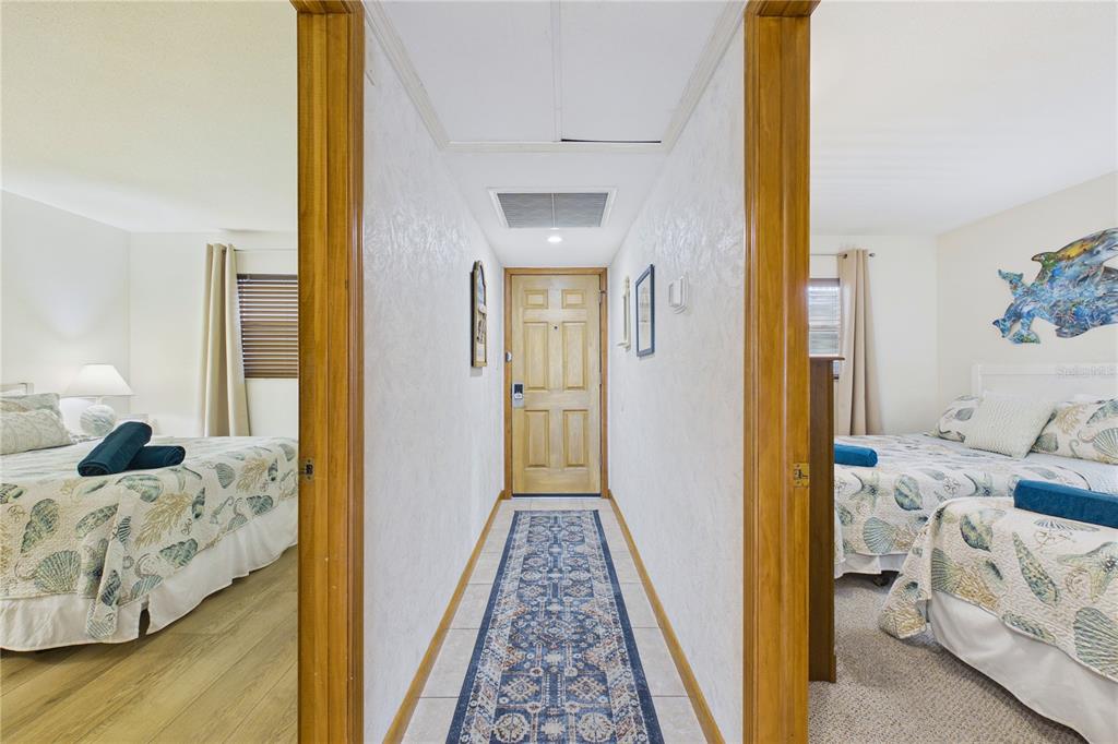 A hallway with a patterned runner rug leads to a wooden door between two bedrooms — 19610 GULF BOULEVARD UNIT 206, INDIAN ROCKS BEACH, FL