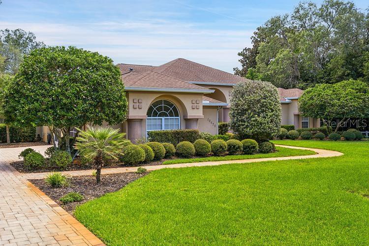 A tan single-story house with a paved driveway and manicured landscaping under a blue sky — 10470 RAMBLE RIDGE COURT, WEEKI WACHEE, FL