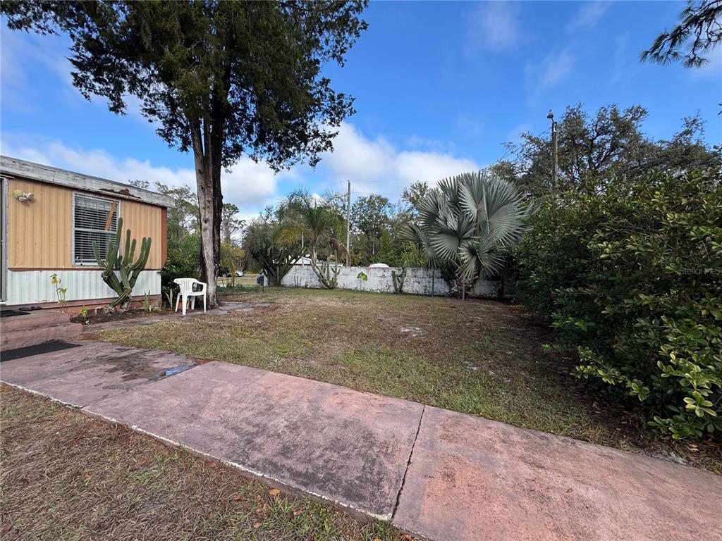A side yard with a concrete walkway, a mobile home, and various trees and shrubs — 12748 VIA PLAZA WAY, NEW PORT RICHEY, FL