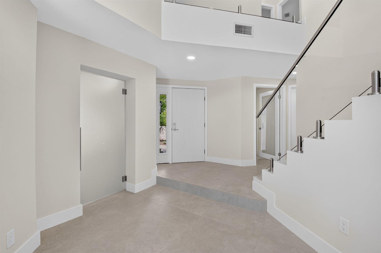A modern foyer features a glass door, a white front door, and a floating staircase — 2103 NW 53rd Street, Boca Raton FL 33496, BOCA RATON, FL