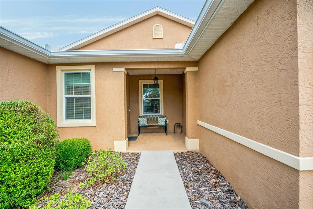 The exterior of a tan stucco house features a covered entryway with a small bench — 9222 SW 97TH CIRCLE, OCALA, FL