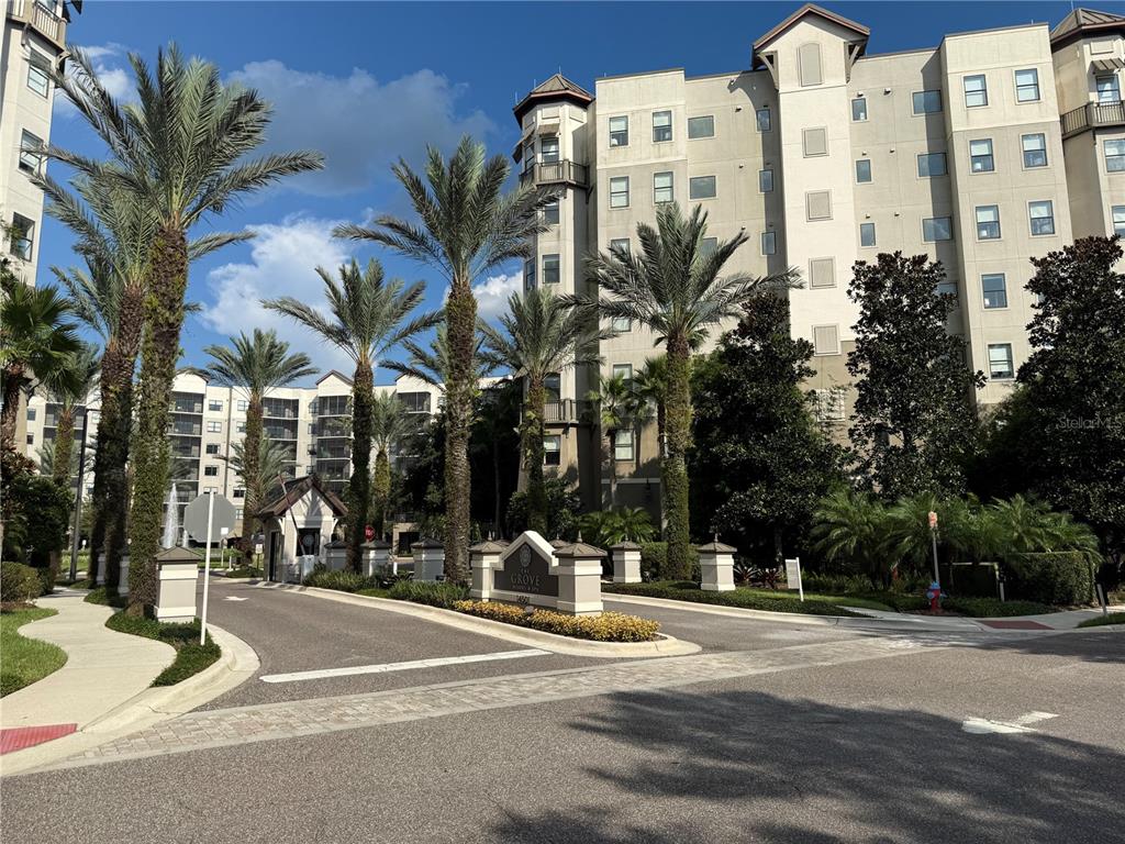 The entrance to a multi-story apartment complex features palm trees and a gated security booth — 14501 GROVE RESORT AVENUE UNIT 1407, WINTER GARDEN, FL