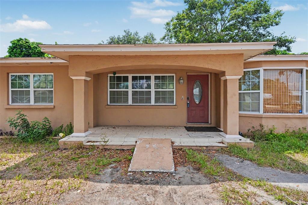 A single-story house with a tan stucco exterior, a covered front porch, and a red door — 1358 S KEENE ROAD, CLEARWATER, FL