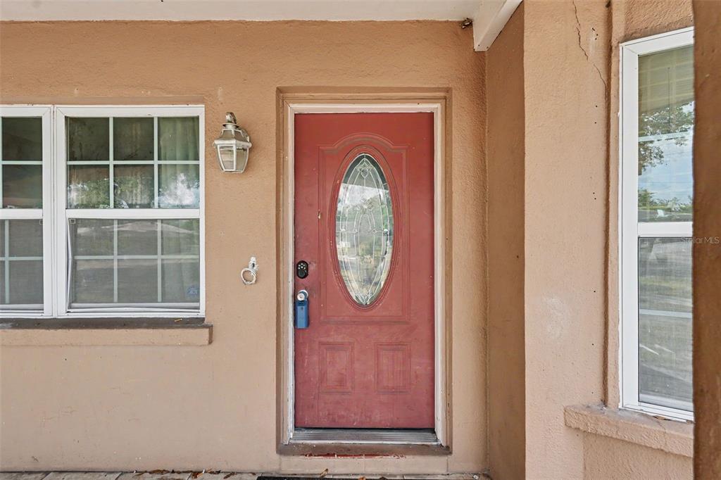 A red front door with an oval glass insert sits between two windows — 1358 S KEENE ROAD, CLEARWATER, FL
