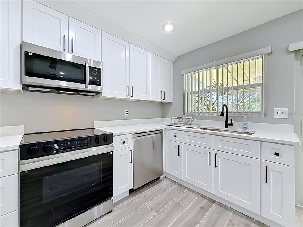A modern kitchen features white cabinets, stainless steel appliances, and gray wood-look tile flooring — 355 BOCA CIEGA POINT BOULEVARD UNIT 355, ST PETERSBURG, FL