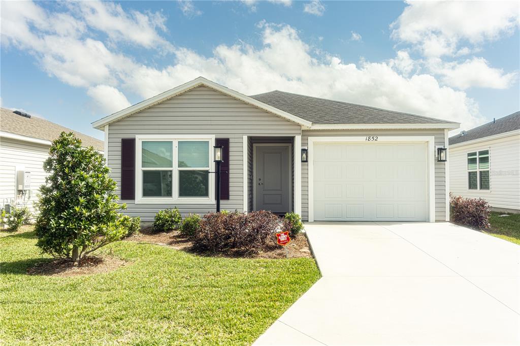 A single-story house with gray siding, a white garage door, and a front lawn — 1852 TIMON STREET, THE VILLAGES, FL