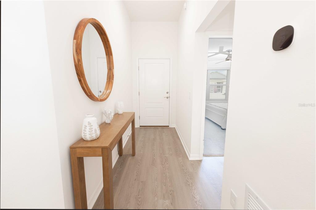 A hallway features light wood-look flooring, a console table with decor, and a round mirror — 1852 TIMON STREET, THE VILLAGES, FL
