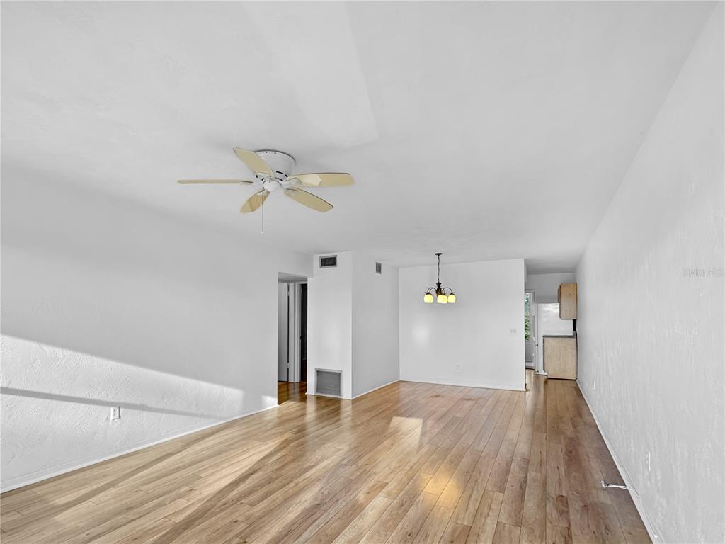 An open-concept living and dining area features white walls, wood-look flooring, and a ceiling fan — 4300 58TH STREET N UNIT 1915, KENNETH CITY, FL