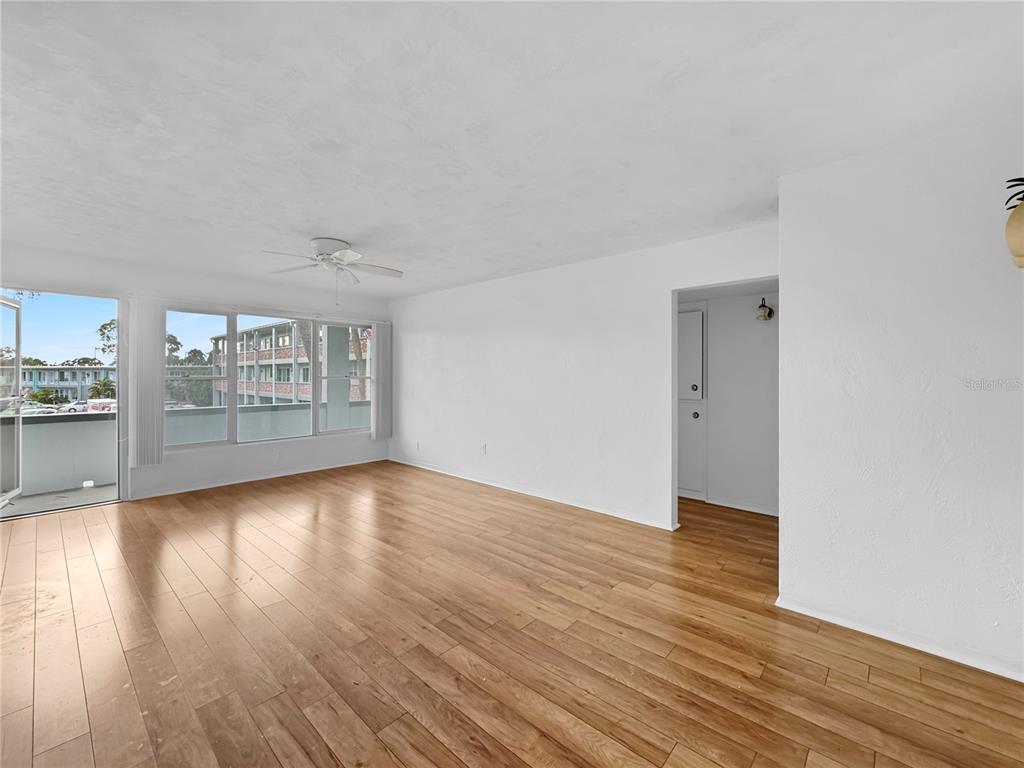 An empty living room features white walls, hardwood floors, a ceiling fan, and a balcony — 4300 58TH STREET N UNIT 1915, KENNETH CITY, FL