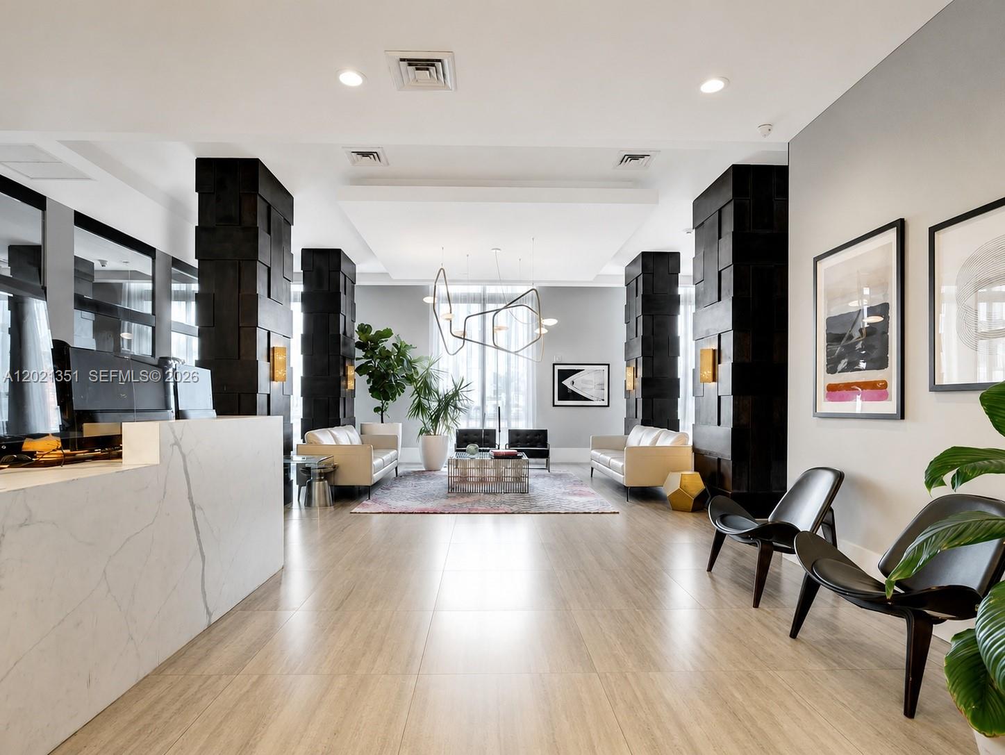 A modern lobby features a marble reception desk, dark wood columns, and contemporary seating areas — 140 S Dixie Hwy # 510, Hollywood FL 33020, HOLLYWOOD, FL