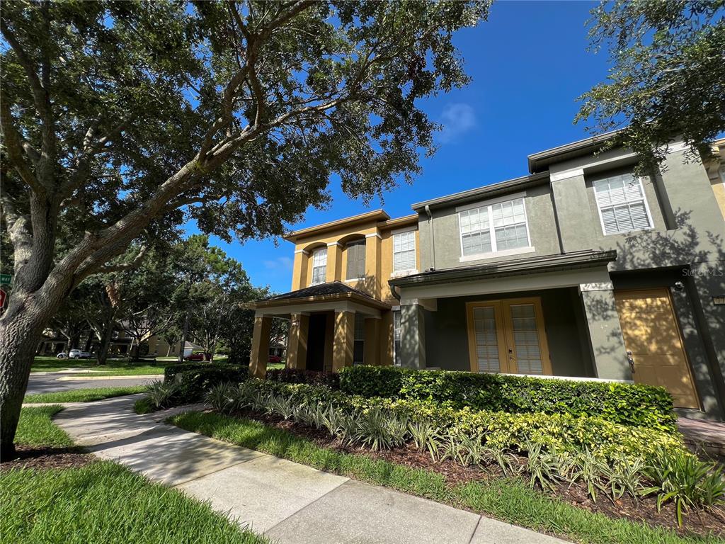 A two-story townhouse with a tan and olive exterior, a front porch, and landscaped garden — 7722 FAIRGROVE AVENUE, WINDERMERE, FL