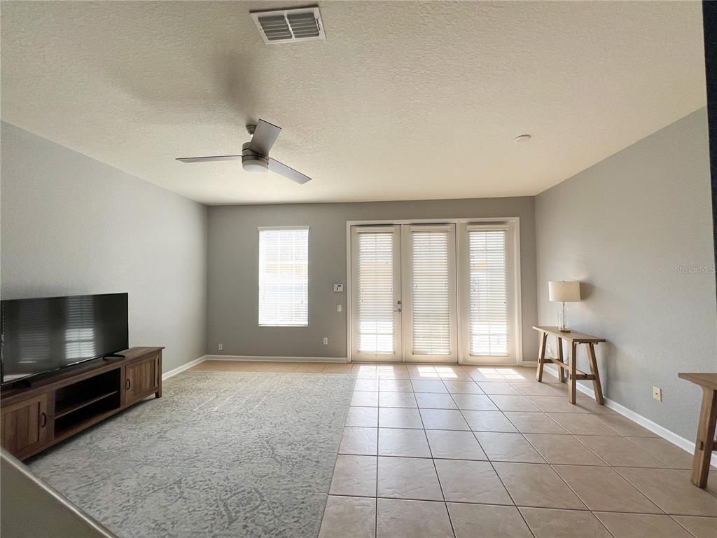 A living room features tile flooring, a ceiling fan, a television console, and glass doors — 7722 FAIRGROVE AVENUE, WINDERMERE, FL