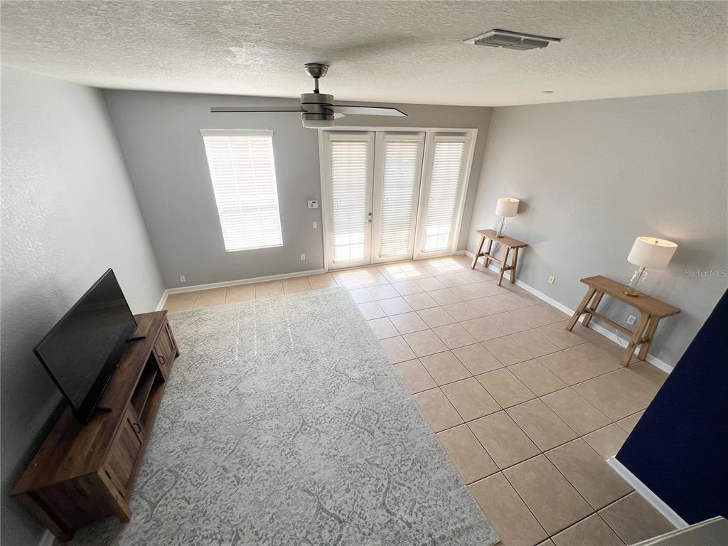 A living room features tile flooring, a large area rug, a television console, and glass doors — 7722 FAIRGROVE AVENUE, WINDERMERE, FL