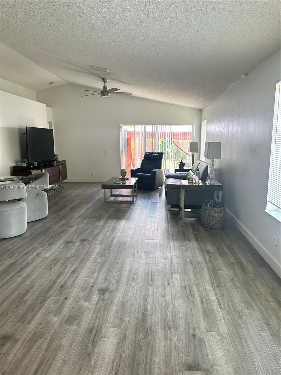 A living room features gray wood-look flooring, a vaulted ceiling, and a sliding glass door — 4025 Pine Ridge Ln, Weston FL 33331, WESTON, FL