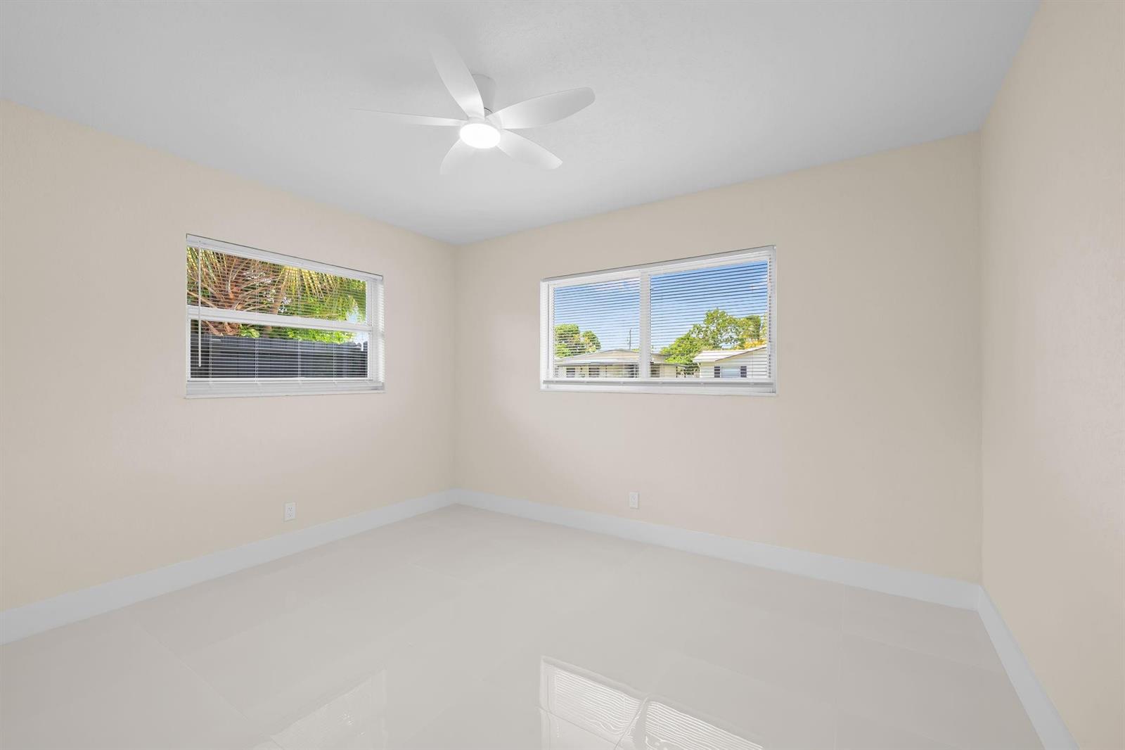An empty bedroom with white tile floors, beige walls, two windows, and a ceiling fan — 832 NE 12th Avenue # 1, Pompano Beach FL 33060, POMPANO BEACH, FL
