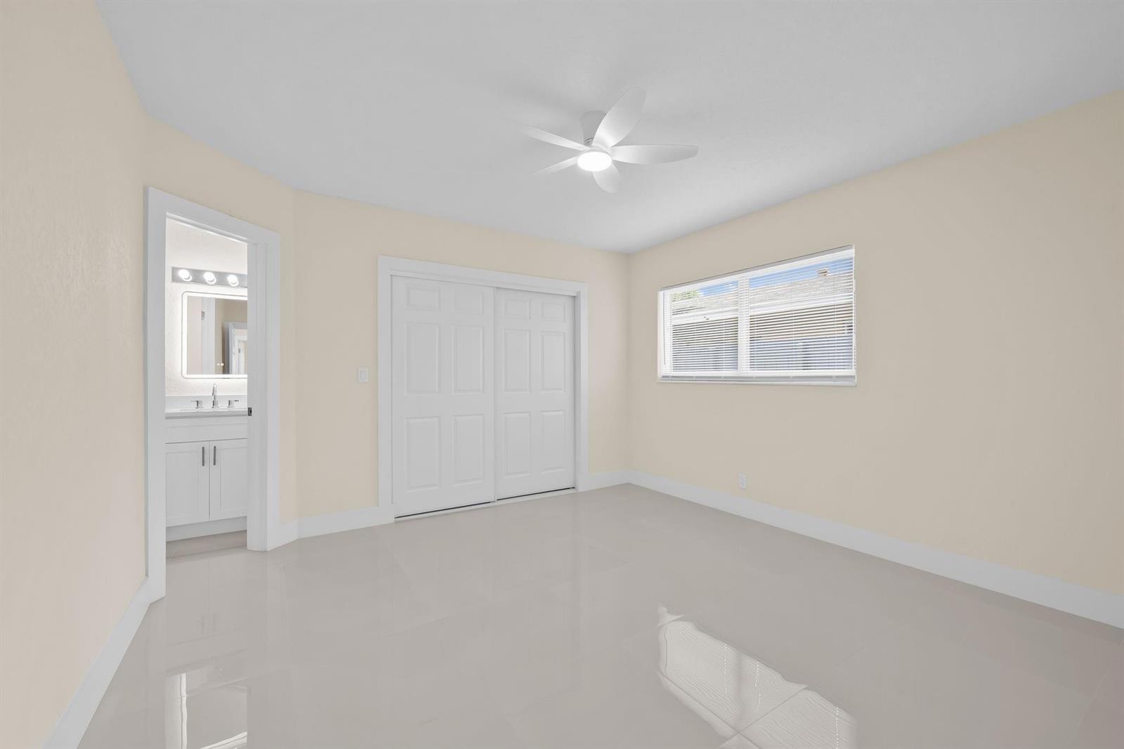 A bright bedroom features light-colored walls, white tile flooring, a ceiling fan, and an attached bathroom — 832 NE 12th Avenue # 1, Pompano Beach FL 33060, POMPANO BEACH, FL