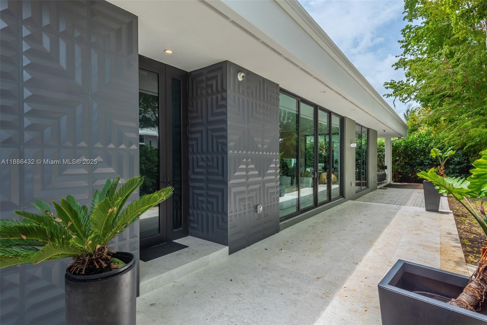 A modern home exterior features textured gray wall panels, large glass doors, and stone flooring — 4675 NE 2nd Ave, Miami FL 33137, MIAMI, FL