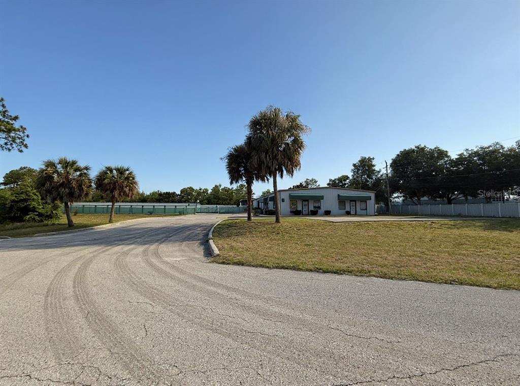 A paved driveway leads toward a single-story commercial building surrounded by palm trees and fencing — 1424 N GULF AVENUE, CRYSTAL RIVER, FL