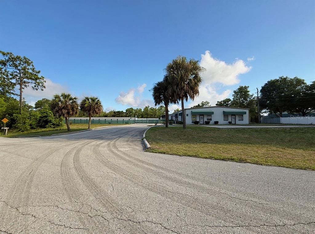 A paved driveway leads toward a commercial building with palm trees and a fenced lot — 1424 N GULF AVENUE, CRYSTAL RIVER, FL