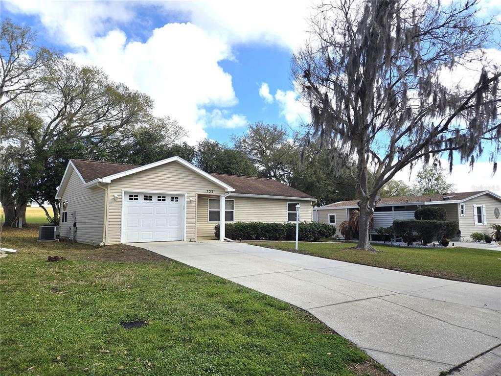 A single-story house with beige siding, a white garage door, and a concrete driveway — 739 HEATHROW AVENUE, LADY LAKE, FL
