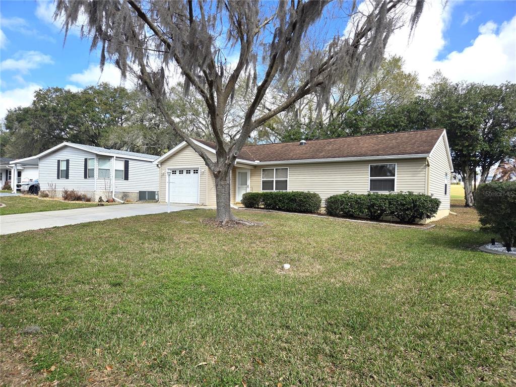 A tan, single-story house with a garage and a large tree in the front yard — 739 HEATHROW AVENUE, LADY LAKE, FL