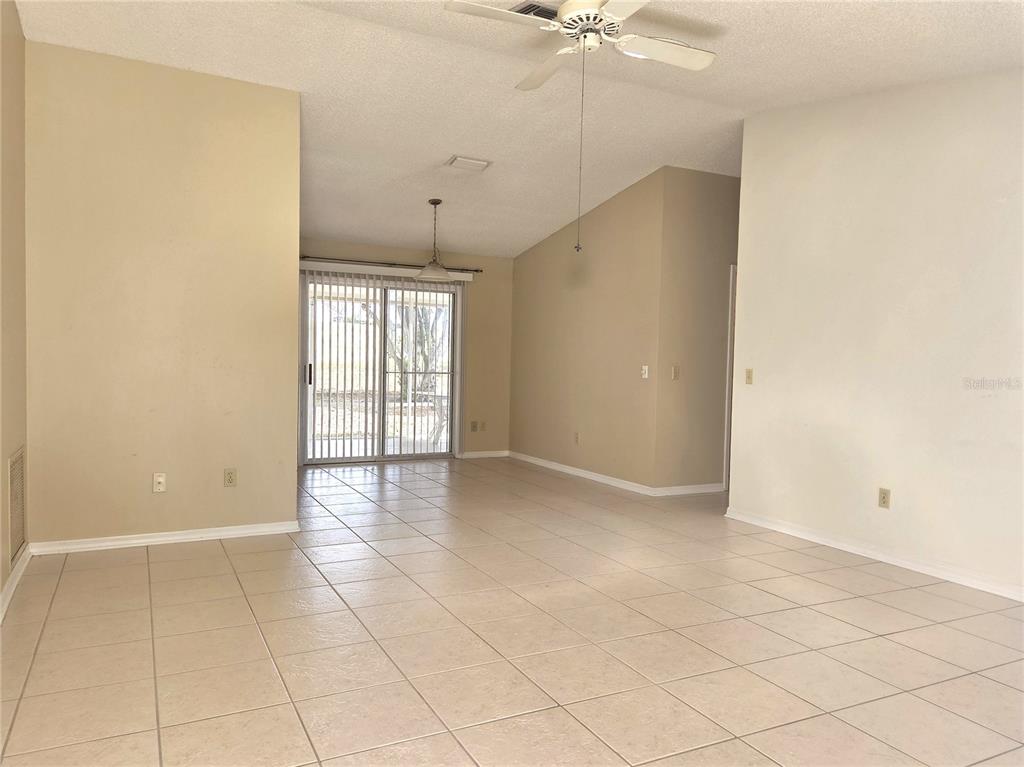 An empty living area features light-colored tile flooring, beige walls, and a sliding glass door — 739 HEATHROW AVENUE, LADY LAKE, FL