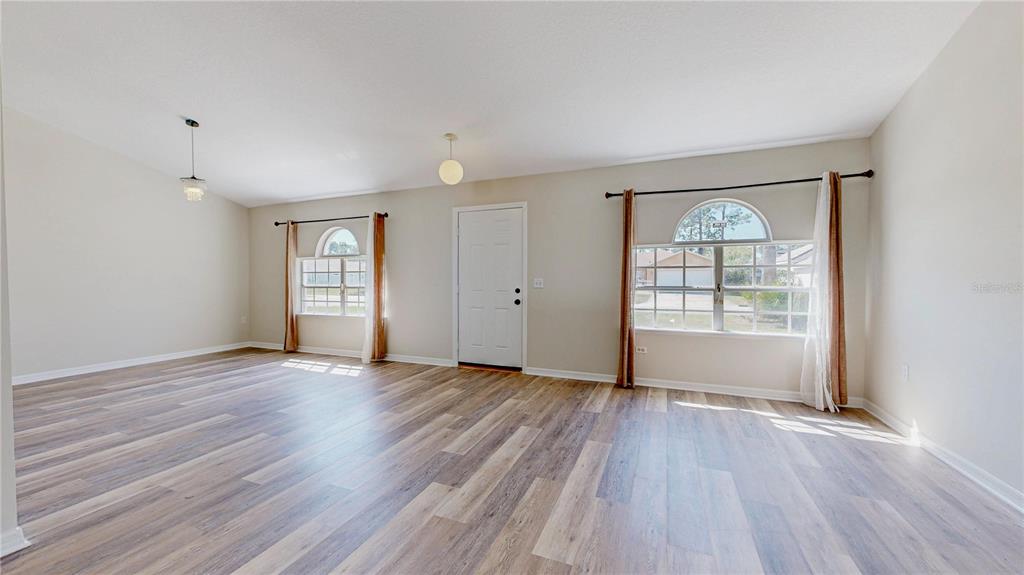 A living room with light-colored walls, wood-look flooring, two arched windows, and a central door — 7 SMOKEHOUSE PLACE, PALM COAST, FL