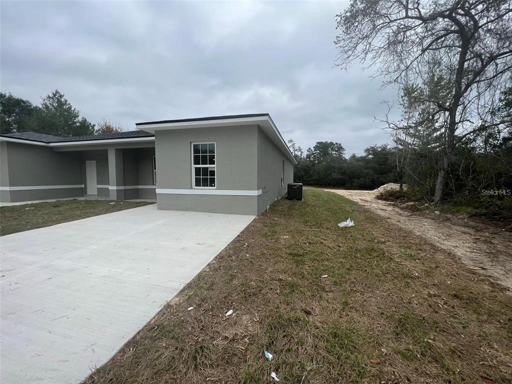 A side view of a gray stucco house with a concrete driveway and adjacent dirt lot — 16170 SW 33RD AVENUE ROAD, OCALA, FL