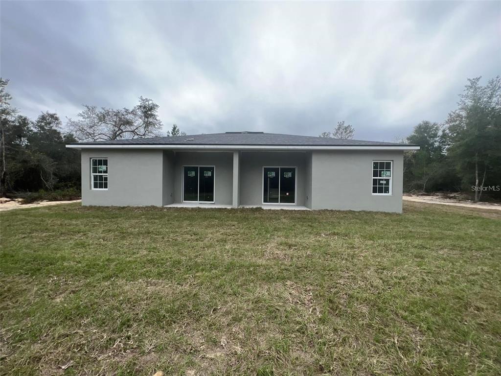 The rear exterior of a gray, single-story house features two sliding glass doors and windows — 16170 SW 33RD AVENUE ROAD, OCALA, FL