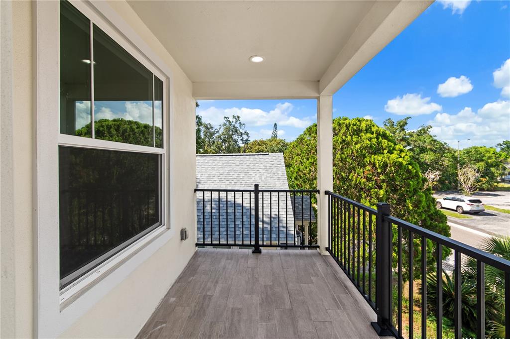 A covered balcony features wood-look tile flooring and a black metal railing overlooking trees — 2141 UPTON COURT S, ST PETERSBURG, FL