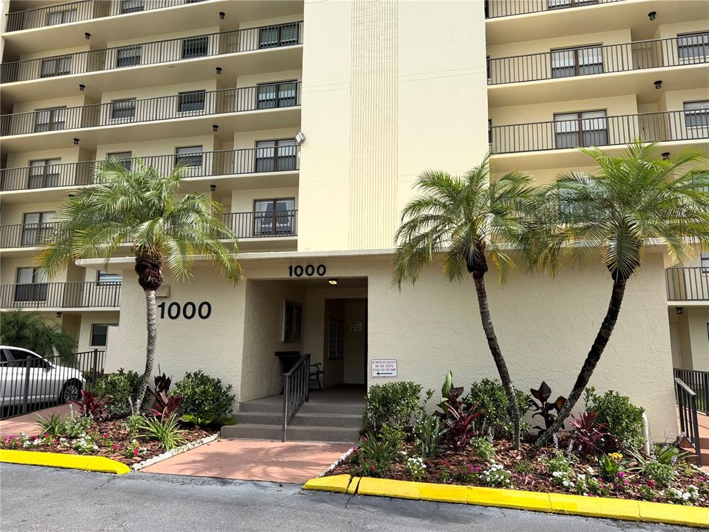 The exterior of a multi-story apartment building features balconies, palm trees, and a ground-level entrance — 1000 COVE CAY DRIVE UNIT 4D, CLEARWATER, FL