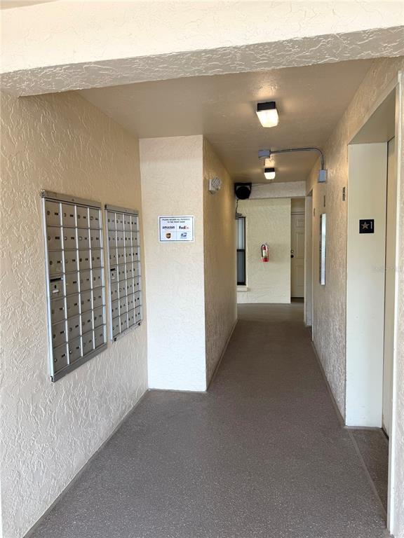 An outdoor apartment hallway features a wall of metal mailboxes and a fire extinguisher — 1000 COVE CAY DRIVE UNIT 4D, CLEARWATER, FL