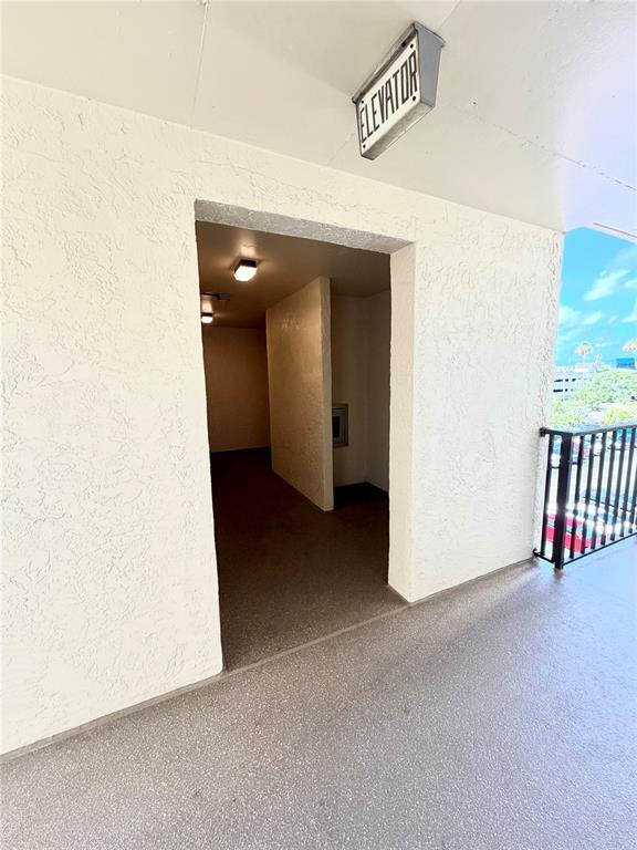 An outdoor walkway leads to an elevator entrance with textured white walls and concrete flooring — 1000 COVE CAY DRIVE UNIT 4D, CLEARWATER, FL