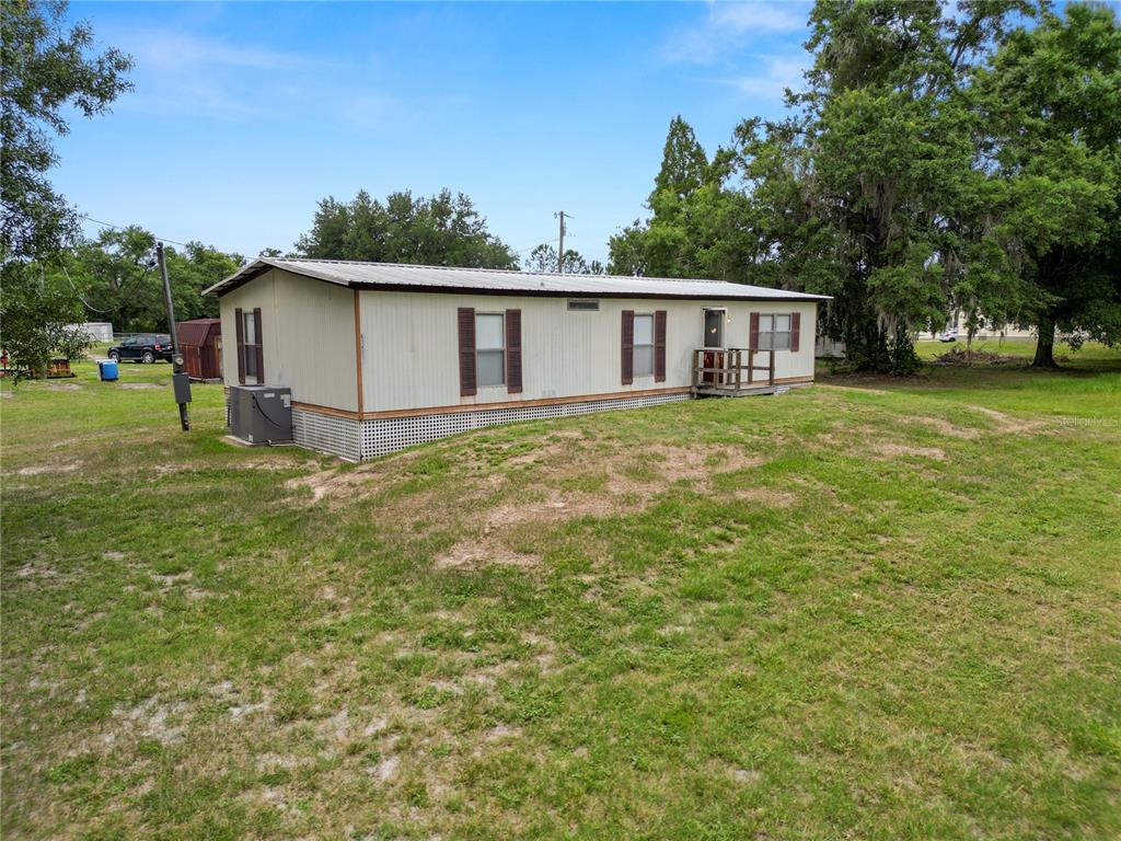 A single-story manufactured home sits on a grassy lot with mature trees in the background — 6216 DOVECREST TRAIL, LAKELAND, FL