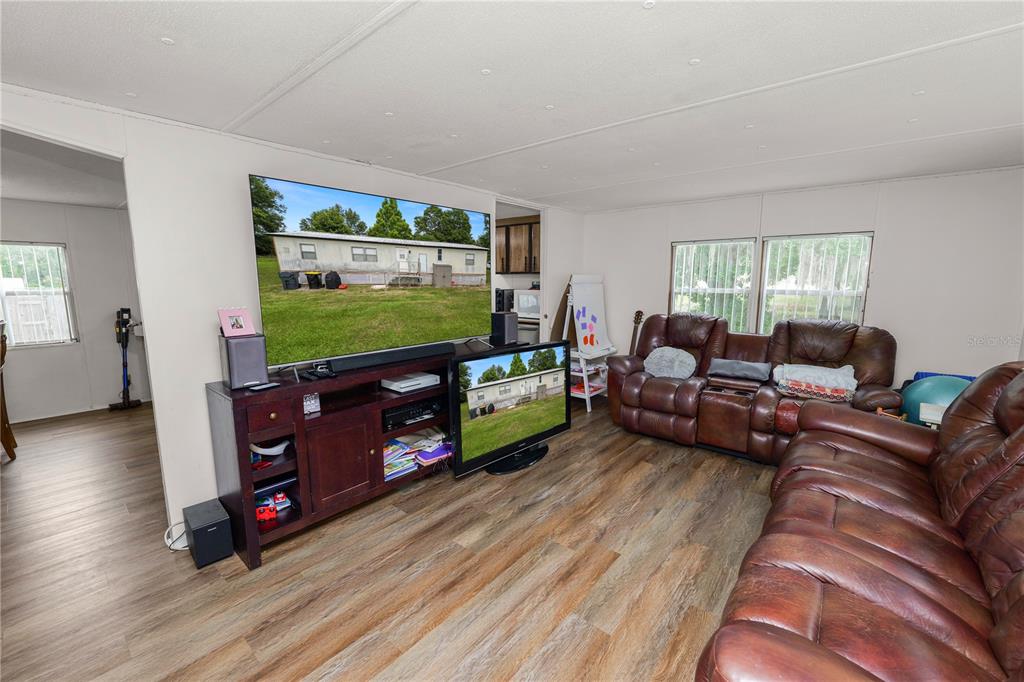 A living room features wood-look flooring, brown leather reclining sofas, and two televisions on stands — 6216 DOVECREST TRAIL, LAKELAND, FL