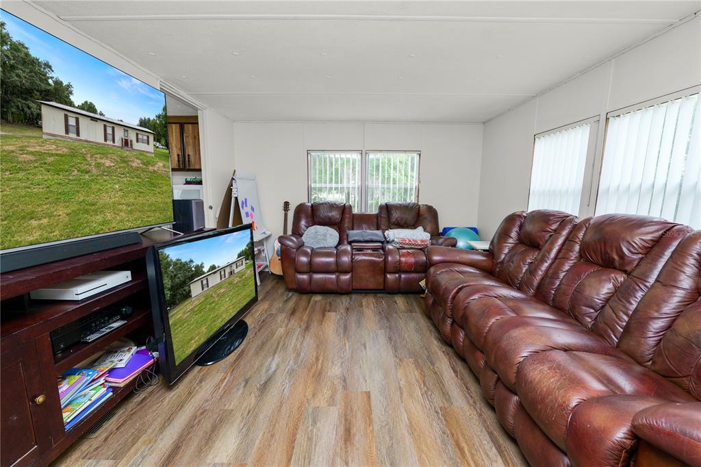 A living room features wood-look flooring, a brown leather sofa, and two televisions — 6216 DOVECREST TRAIL, LAKELAND, FL