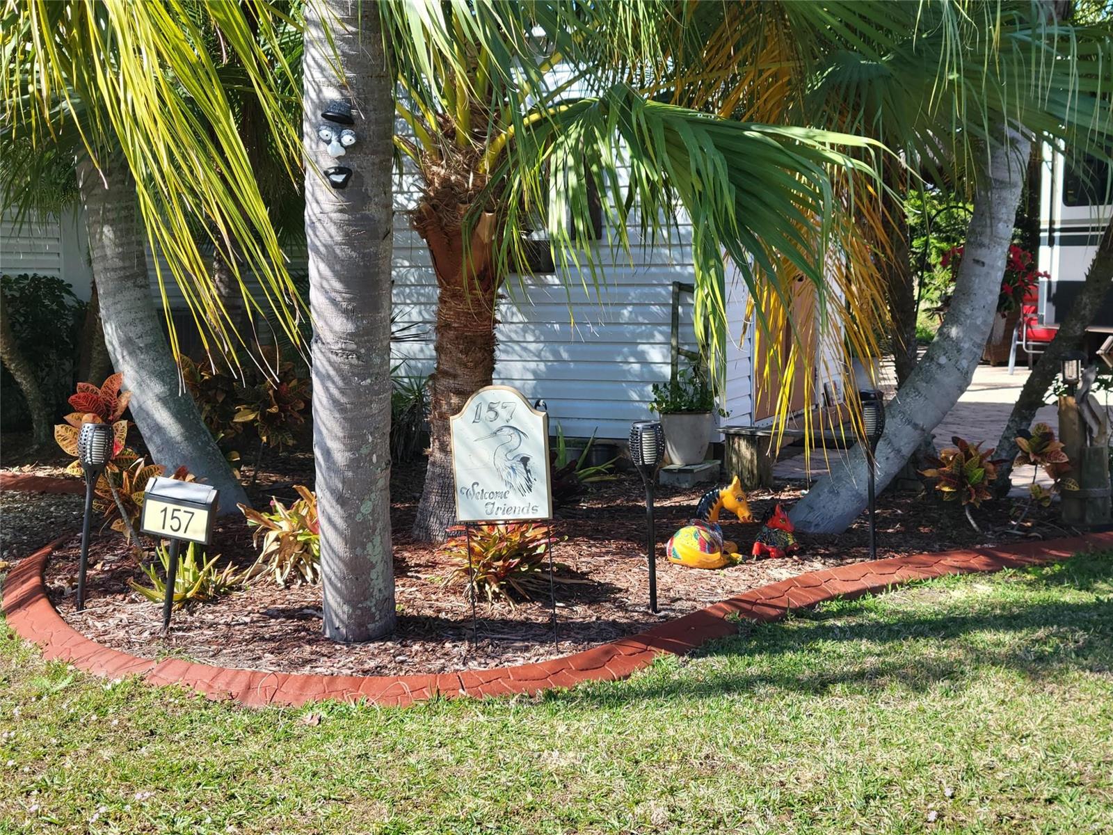A landscaped garden bed features palm trees, a house number sign, and decorative lawn ornaments — 3755 SE 6th Glen, Okeechobee FL 34974, OKEECHOBEE, FL