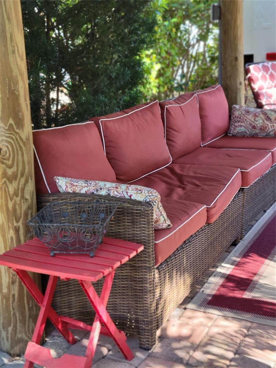 A wicker outdoor sofa with red cushions sits on a patio next to a small table — 3755 SE 6th Glen, Okeechobee FL 34974, OKEECHOBEE, FL