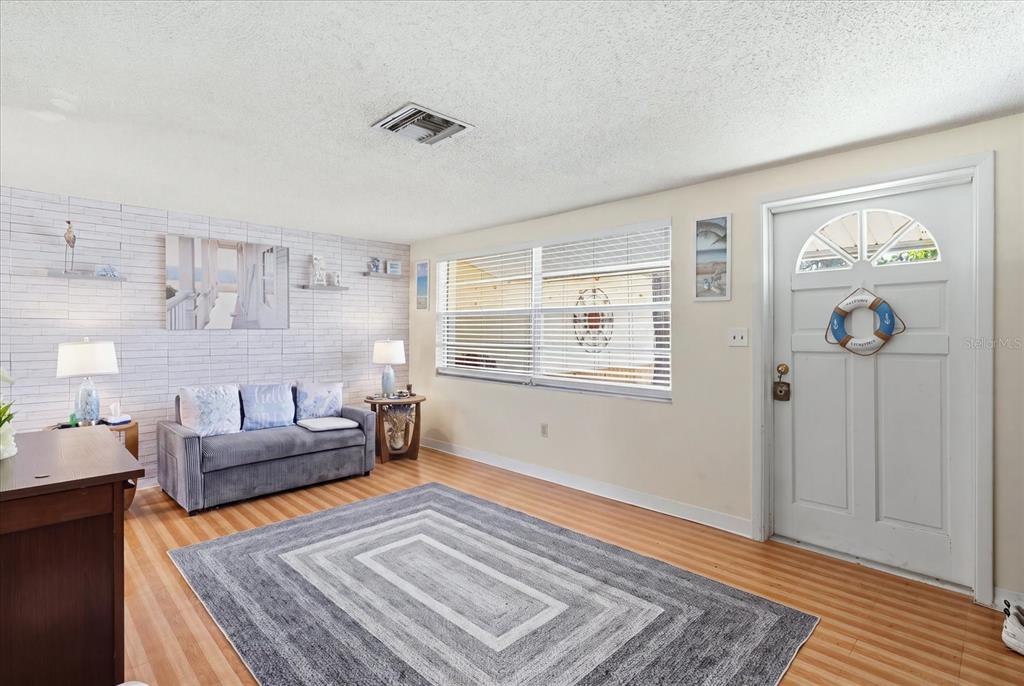 A living room features light wood flooring, a gray sofa, and a white brick-patterned wall — 1149 N TRUDEL POINT, CRYSTAL RIVER, FL