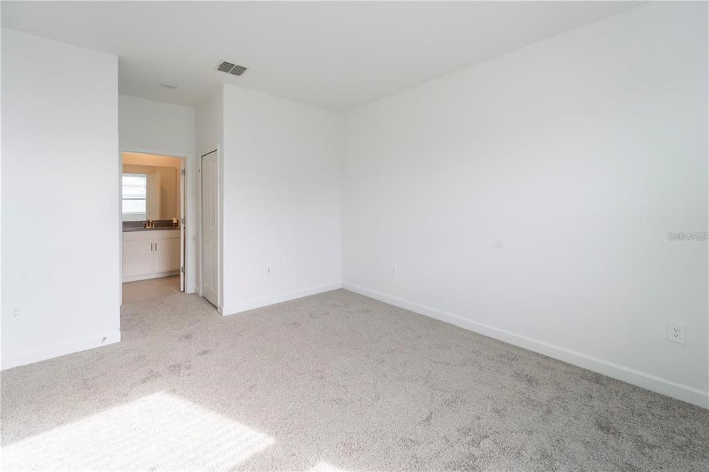 A bedroom with white walls, gray carpet, and an open doorway leading to a bathroom — 4032 REDBRIDGE LOOP, DAVENPORT, FL