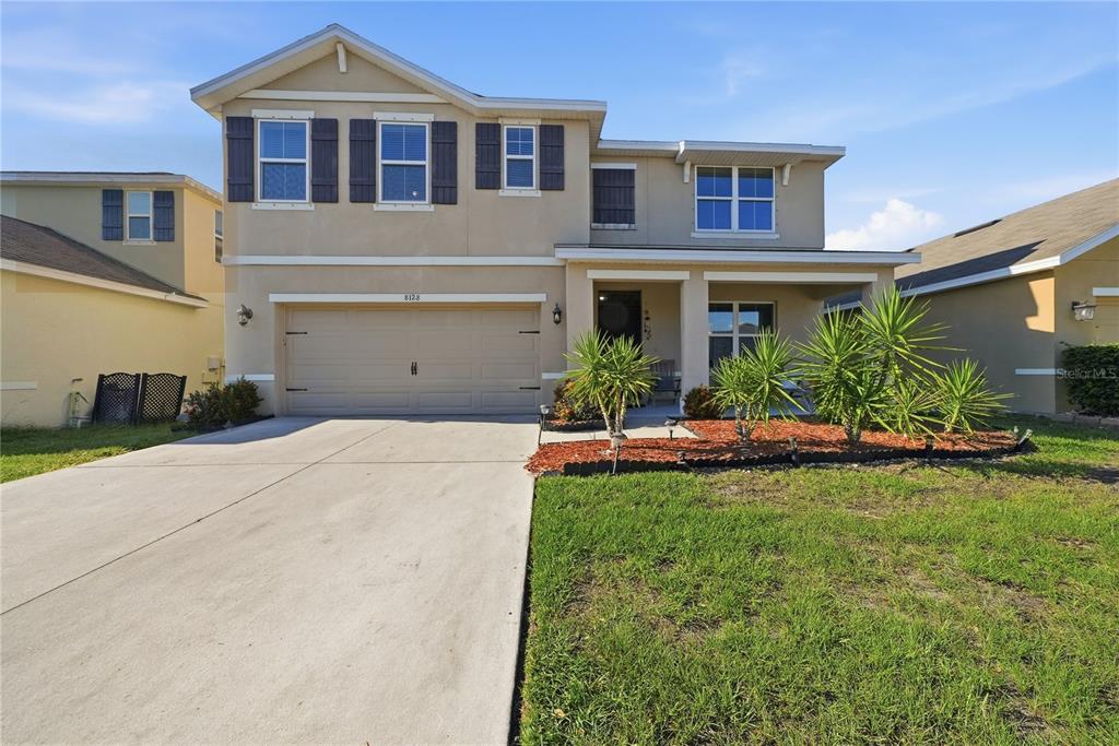 A two-story suburban house features a tan stucco exterior, a two-car garage, and a front porch — 8128 HARWICH PORT LANE, GIBSONTON, FL